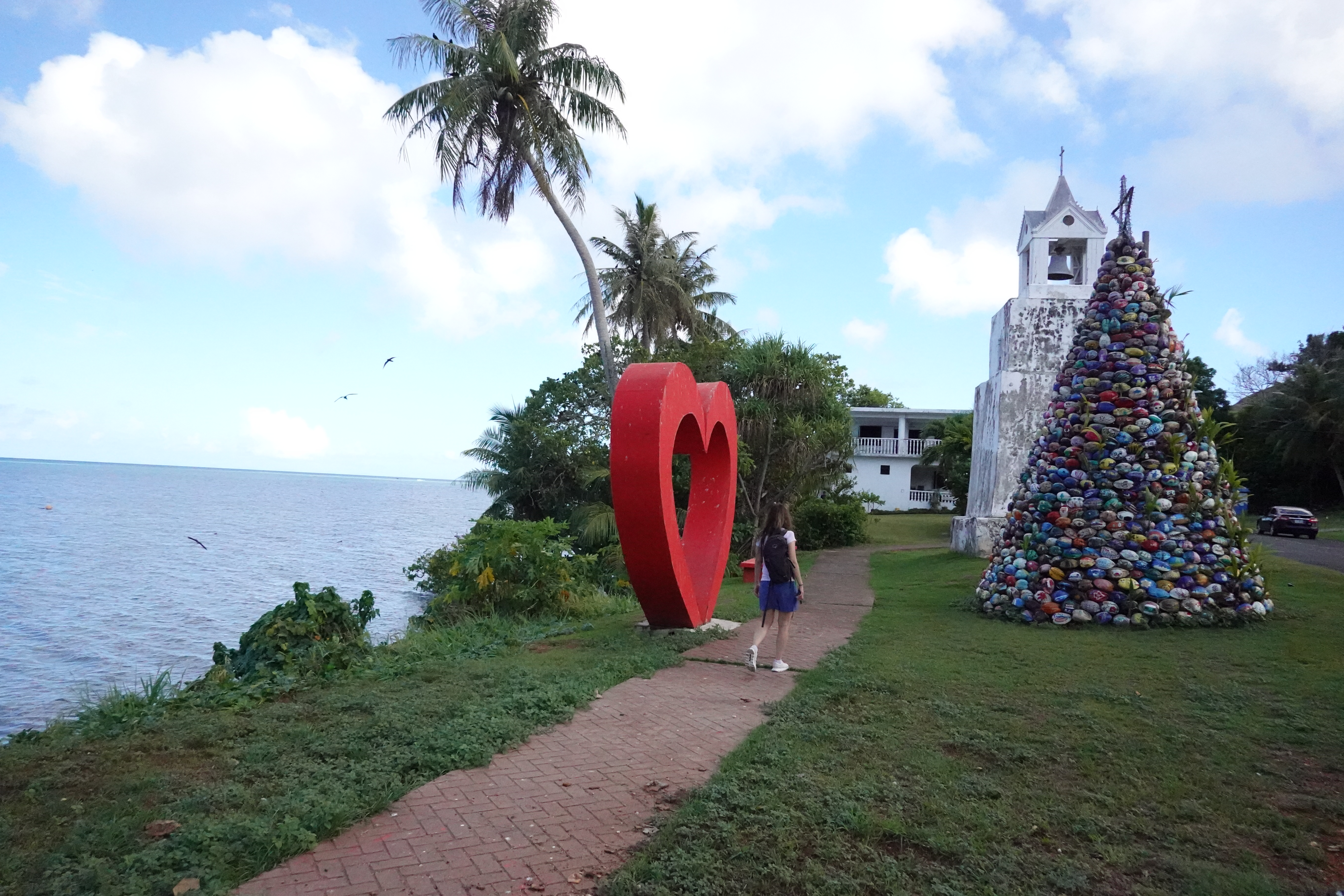 Annette, walking between a heart-shaped statue(?) and a tall christmas tree-like pile of hand-painted coconuts. In
