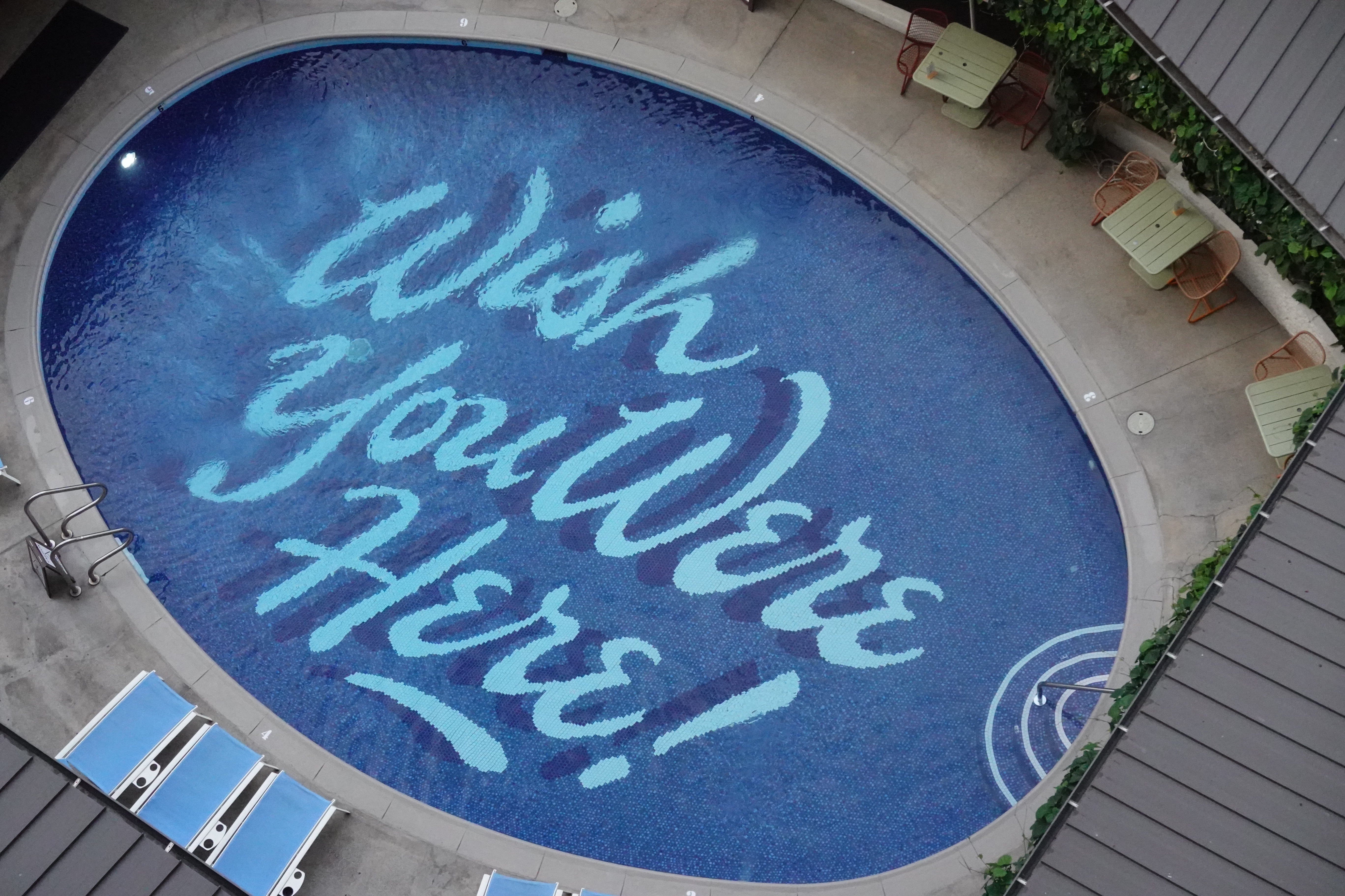 birds-eye photo of a pool with a floor with script lettering which reads 'Wish you were here'